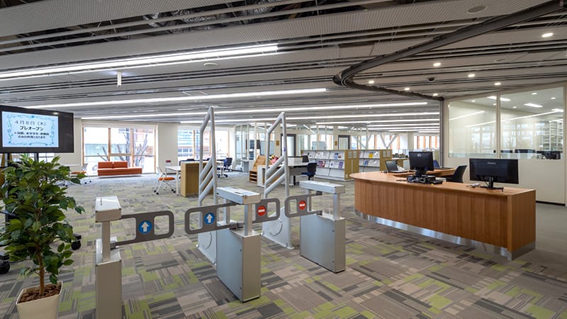 駅前キャンパスの図書室内、入退室ゲートとカウンターが見える明るい空間。