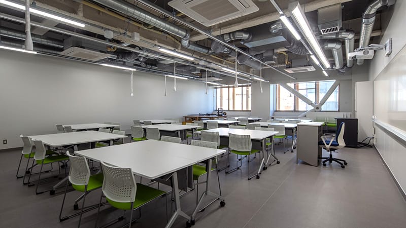 基礎作業実習室の内部、白いテーブルと緑の椅子が並ぶ明るい教室。