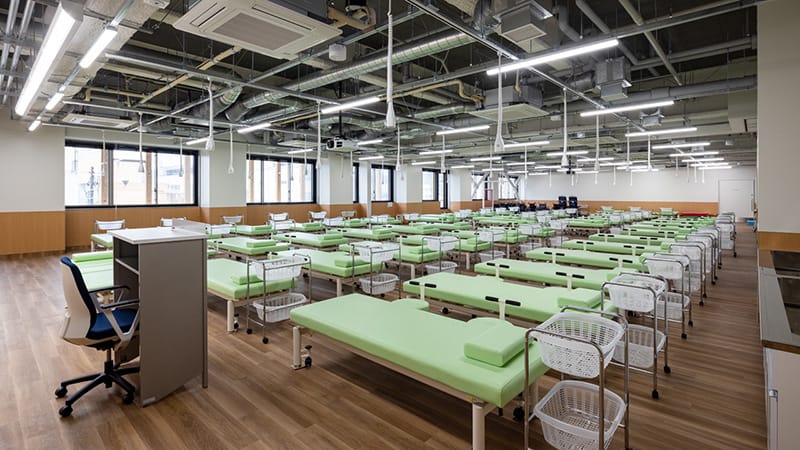 理学療法評価室の広々とした室内、緑のベッドが整然と並ぶ。