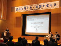 福島医学会のシンポジウムで講演を行う医師と聴衆の様子、背景には「医師を育てる・医師を支える」の横断幕。