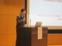 福島医学会のシンポジウムで講演を行う講師が、マイクを持って話している様子。