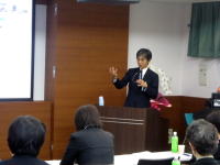 福島県立医科大学での講演中の男性が、聴衆に向かって話している様子。