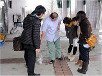 災害医療研修の一環として、数人の参加者が指導者の説明を受けながら地面を見つめている様子。