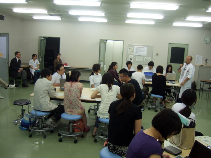 セミナーで講演を行う医師と、参加者が集まる教室の様子。