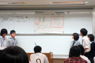 医療系セミナーで発表を行う学生たちが、ホワイトボードの資料を指し示している様子。