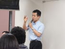 医療系セミナーで講演を行う男性がマイクを持ち、参加者に向けて話している様子。