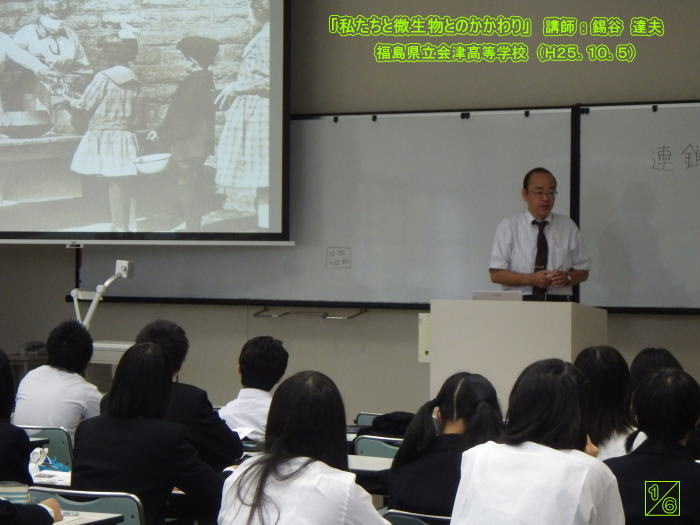 出前講座で講演する講師と、後方に映る歴史的な写真を見つめる生徒たち。福島県立会津高等学校での様子。