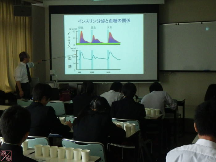 出前講座で講師がインスリン分泌と血糖の関係について説明している様子。学生たちが聴講している教室の風景。