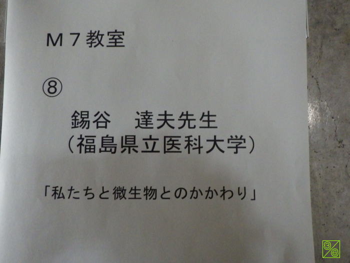M7教室の掲示板に、鎌谷達夫先生（福島県立医科大学）の講義タイトル「私たちと微生物とのかかわり」が記載された紙。