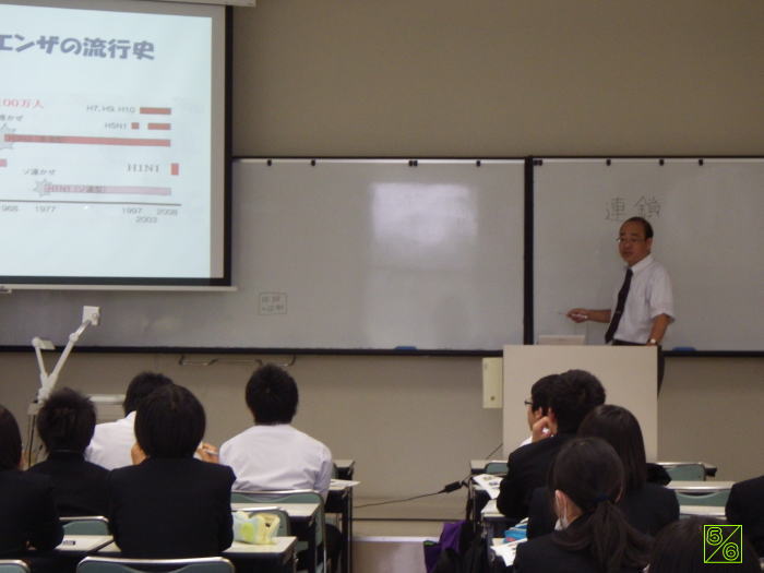 出前講座で講義を行う講師と、受講生たちが座っている教室の様子。ホワイトボードにはプレゼンテーション資料が映し出されている。