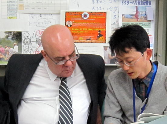 法務安全保障省危機管理局長のNestor Alejandro Nicolas氏と、別の男性が資料を見ながら話し合っている様子。背景には掲示物やメモが貼られた壁が見える。