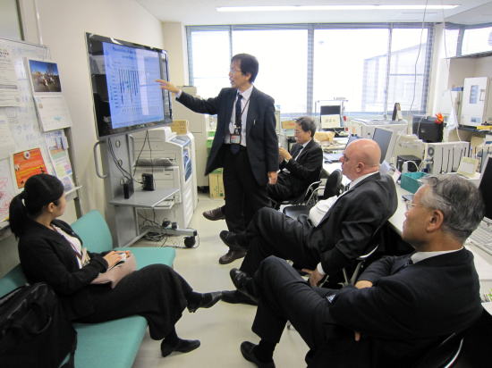 医療機関の会議室で、数名のビジネスマンがプレゼンテーションを受けている様子。
