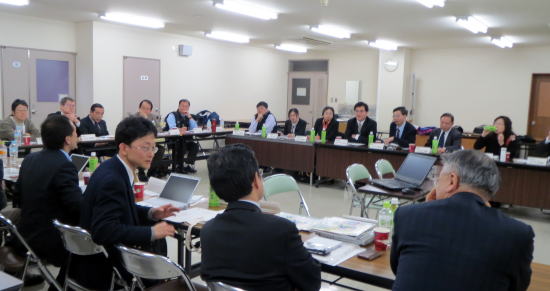 会議室でのディスカッションに参加する多くの人々が座っている様子。テーブルには資料や飲み物が並んでいる。
