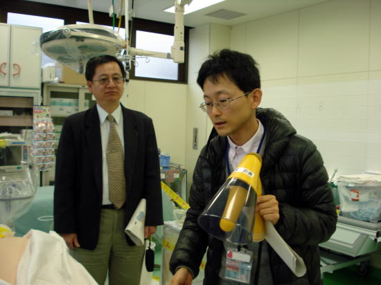医療現場での説明を行う男性と、その様子を見守る男性が写っている。