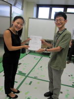 福島県立医科大学での表彰式で、男性と女性が証書を手に笑顔で向き合っている様子。