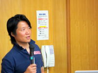 福島災害医療セミナーで講演する男性がマイクを持ち、聴衆に向けて話している様子。