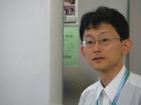 福島県立医科大学の研究室で、白いシャツを着た男性がカメラを見つめている様子。