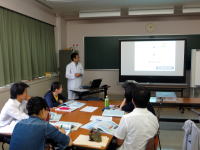 医療に関するプレゼンテーションを行う講師と、聴講する学生たちがいる教室の様子。