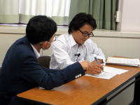 医療に関する相談を行っている二人の男性が、テーブルに向かい合って話し合っている様子。