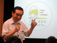福島県立医科大学の講演で話す男性がマイクを持ち、背景には「未来を創る教育」というロゴが見える。