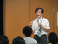 福島県立医科大学で講演を行う男性が、聴衆に向かって話している様子。