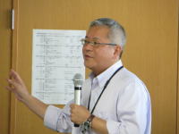 福島県立医科大学で講演を行う男性がマイクを持ち、話している様子。背景には掲示物が見える。