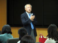 福島県立医科大学で講演を行う男性がマイクを持ち、聴衆に向かって話している様子。
