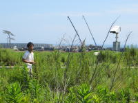 福島県の自然の中で立つ男性と、背景に見える工事現場の風景。