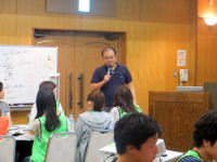 福島県立医科大学の講義中、講師が学生に向かって話している様子。学生たちは緑のTシャツを着ている。