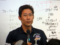講演中の男性がマイクを持ち、ホワイトボードの前で話している様子。