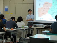 福島県立医科大学の教室で、講師が地図を使って説明している様子。学生たちが真剣に聞き入っている。