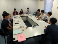 大学の会議室で、学生たちが円卓を囲んで話し合いをしている様子。