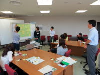 会議室でプレゼンテーションを行う人々の様子。参加者が資料を見ながら意見を交わしている。