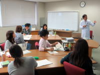 医療に関する講義を受ける学生たちと、説明を行う講師がいる教室の様子。