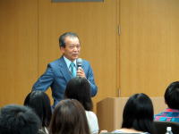 福島県立医科大学で講演を行う男性がマイクを持ち、聴衆に向かって話している様子。