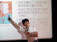 講演中の男性がスライドを指差し、放射線に関する情報を説明している様子。