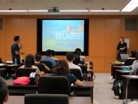 大学の教室でプレゼンテーションを行う学生と聴衆の様子。スクリーンには「BELARUS」と表示されている。