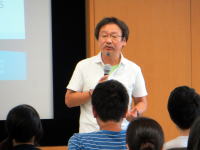 福島県立医科大学で講演を行う男性が、聴衆に向かって話している様子。