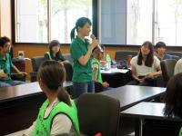 福島県立医科大学の教室で、緑のTシャツを着た女性がマイクを持って話している様子。周囲には学生たちが座っている。