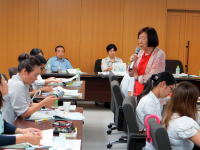 福島県立医科大学の会議室で、講演を行う女性と参加者たちが真剣に聴講している様子。