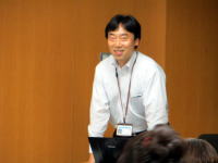 福島県立医科大学で講演を行う男性が、聴衆に向かって微笑んでいる様子。