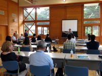 福島県立医科大学の講義室で、参加者が講演を聴いている様子。木製の内装が特徴的な空間。