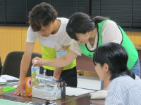 学生が実験器具を使って作業を行っている様子。緑のエプロンを着た2人が協力している。