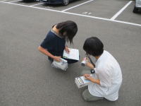 駐車場で資料を確認しながら作業をする二人の学生。