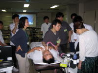 甲状腺超音波検査を受ける男性と、その周囲で指導を受ける医学生たちの様子。