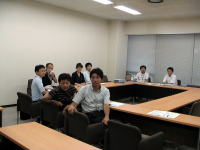 会議室で座っている数人の人々が、テーブルを囲んで話し合っている様子。