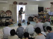 医療に関する講義を受ける参加者たちが、講師の説明を聞いている様子。背景には医療関連の道具や資料が並んでいる。