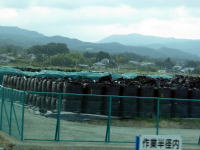 福島県の風景に囲まれた、黒い袋が積まれた作業現場の様子。