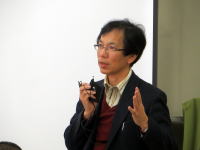 講習中に話をする男性が手を挙げている様子。背景にはホワイトボードが見える。