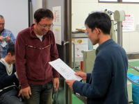 福島県立医科大学での授賞式の様子。男性が書類を手に持ち、別の男性に向かって話している。